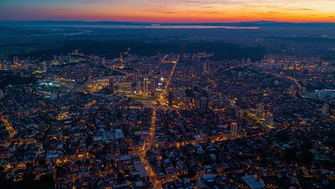 Dusk aerial cityscape with illuminated street grid and coastal horizon at sunset