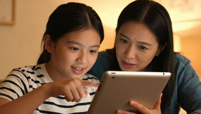 Mother and daughter sharing tablet on sofa, learning together in cozy home