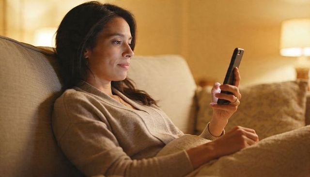 Relaxing woman on sofa using smartphone under warm lamp light for evening leisure