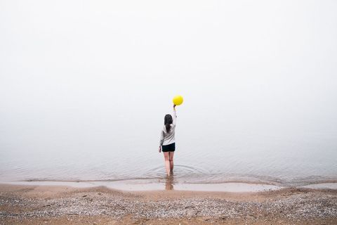 Woman Holding Yellow Balloon at Foggy Beach Shore