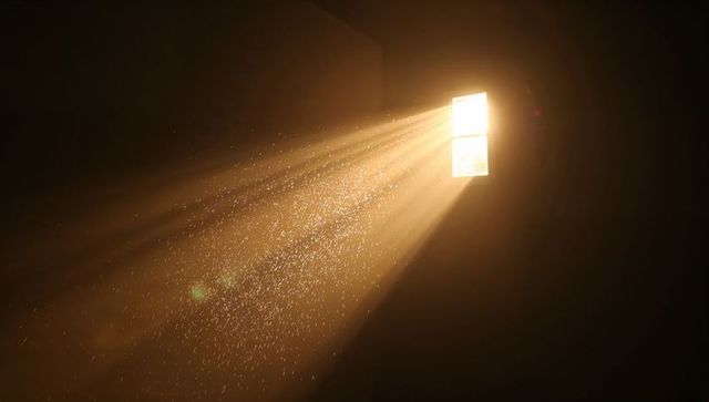 Golden sunbeam streaming through window illuminating floating dust motes in dark room