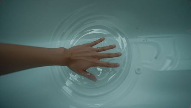 Pressing hand into shallow aqua water creating gentle ripples with slim silver ring