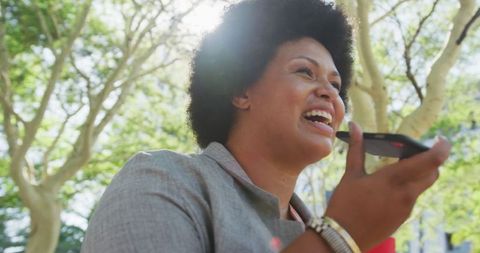 Smiling Woman Enjoying Voice Communication in Sunlit Park