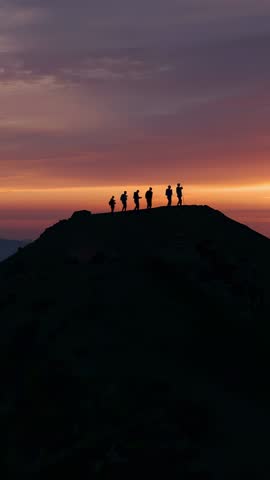 Vertical video of seven hikers silhouetted on ridge at sunrise capturing horizon glow