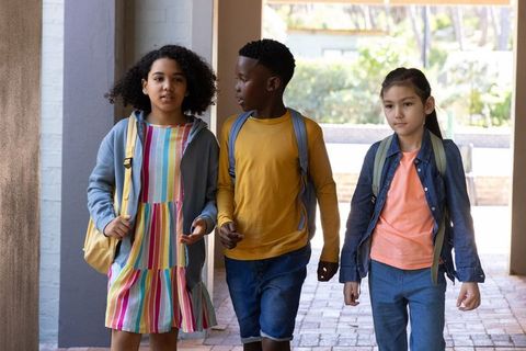 Diverse children walking to school through campus archway carrying backpacks
