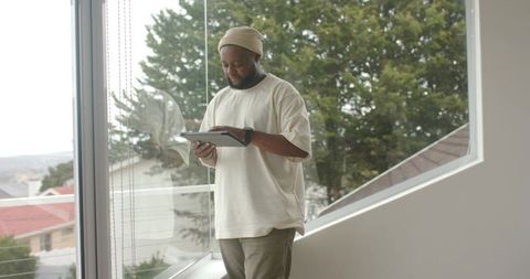 African american man using tablet by floor-to-ceiling window modern interior teleworking