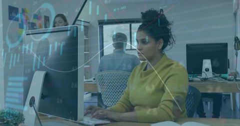 Woman in mustard sweater analyzing data on desktop in open office with chart overlay