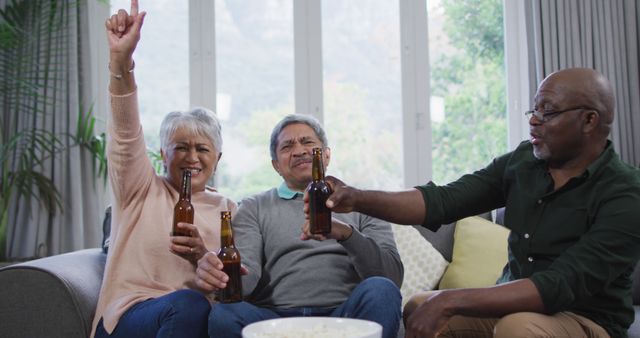 Senior friends are drinking beer and celebrating together indoors, showcasing a joyful and cheerful moment of togetherness. Ideal for use in materials promoting social events, senior social activities, advertisements for retirement communities, or lifestyle content aimed at mature adults enjoying life.