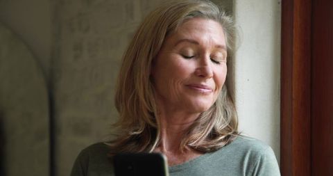 Mature Woman Relaxing by Window with Smartphone at Home