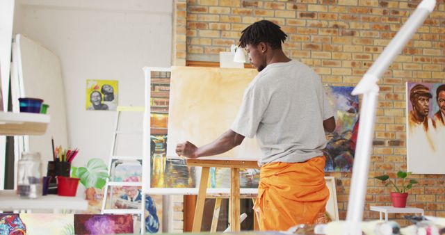 African American artist painting on canvas in a modern, vibrant studio. The artist is deeply focused on his work, with art supplies and paintings around the room. Ideal for use in articles about creativity, arts and culture, inspiration, modern art, or showcasing artistic talent.
