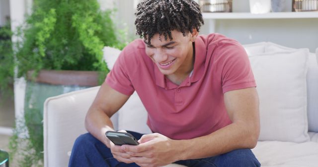 Young man smiling while using smartphone on cozy sofa - Download Free Stock Images Pikwizard.com