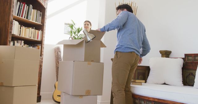 Couple diligently packing moving boxes in a bright living room. Proactively preparing for a move into a new home. Ideal for use in articles or advertisements discussing moving, home relocation tips, or new homeowner experiences.