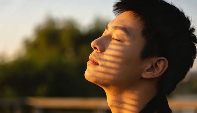 Asian man basking in golden hour light with dramatic shadow stripes on face