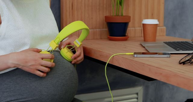 Pregnant Woman Holding Headphones Against Belly Sitting at Workspace - Download Free Stock Images Pikwizard.com