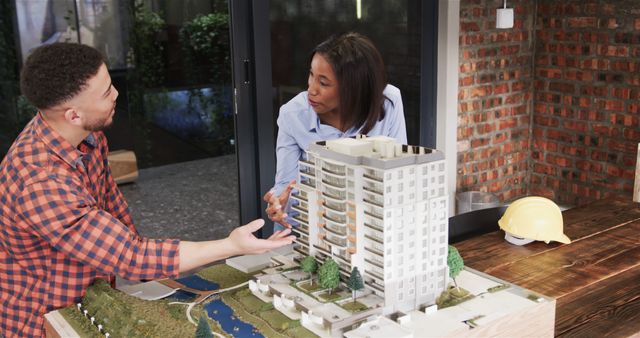 Architects reviewing a model of a high-rise building in a contemporary office with a brick wall background. Perfect for illustrating teamwork, collaboration, and planning in architecture and construction projects. Great for use in articles about architectural design, engineering, project management, or corporate professional environments.