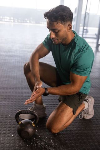 Man kneeling in gym training with kettlebell chalk preparation
