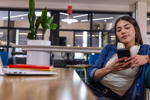 Young woman relaxing with smartphone and headphones at modern coworking table