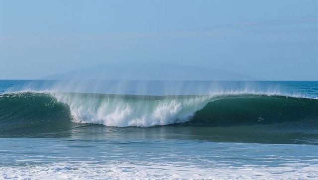 Serene ocean wave breaking into misty barrel at coastline