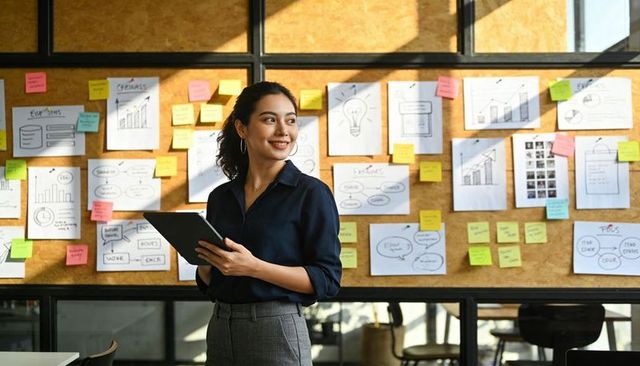 Businesswoman holding tablet reviewing strategy board with sticky notes in bright office