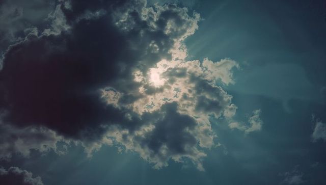 Sun Rays Peeking Through Dramatic Cumulus Clouds in Open Sky