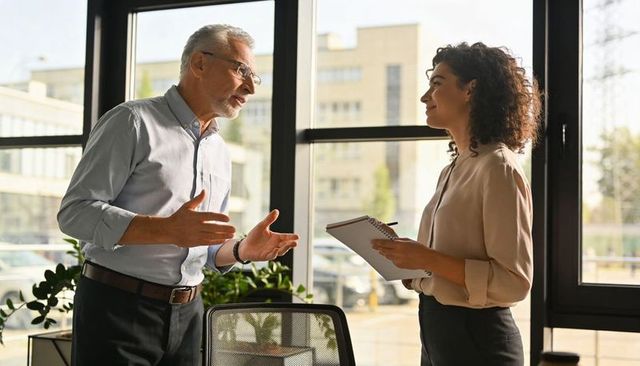 Senior manager and young professional discussing strategy beside bright office windows