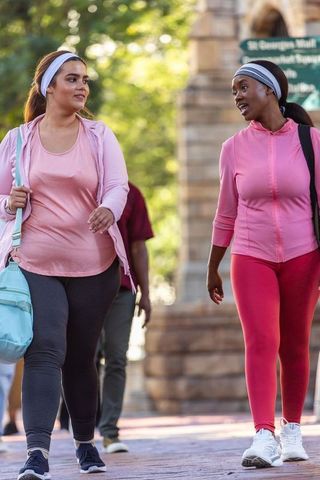 African american friends walking and talking in park wearing pink activewear
