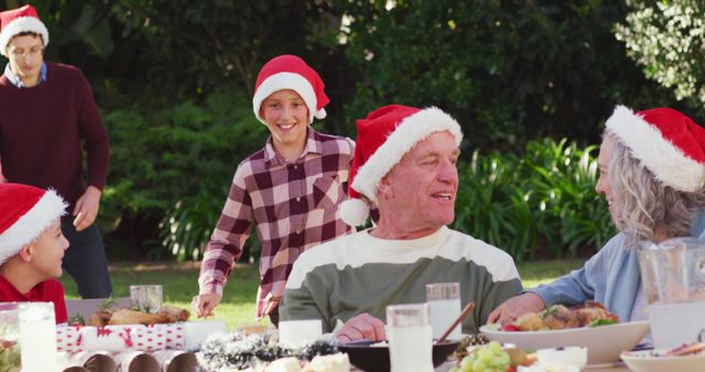 Family gathering outdoors to celebrate Christmas, all members wearing Santa hats with joy and laughter. Perfect for promoting family values, holiday celebrations, Christmas advertisements, greeting cards, and social media posts highlighting festive family activities.