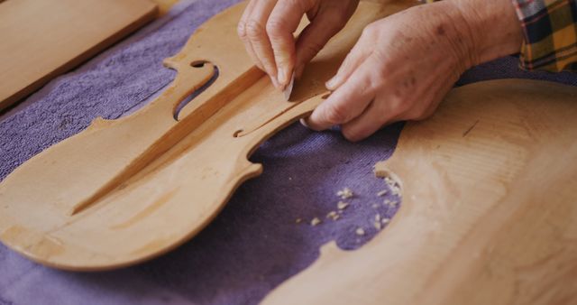 Hands of a luthier assembling top plate of a violin on a workbench. This is great for use in articles about traditional craftsmanship, handmade musical instruments, and precision woodworking. Perfect for illustrating the art of lutherie and the meticulous work involved.