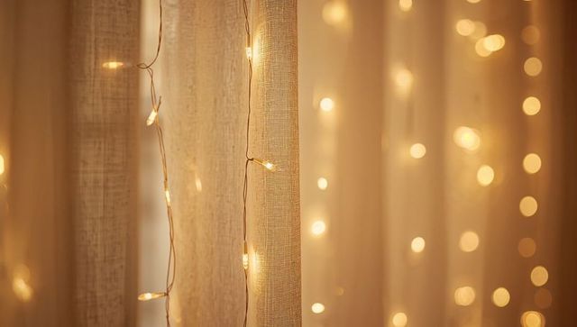 Warm fairy lights on sheer beige curtains creating cozy golden bokeh backdrop interiors