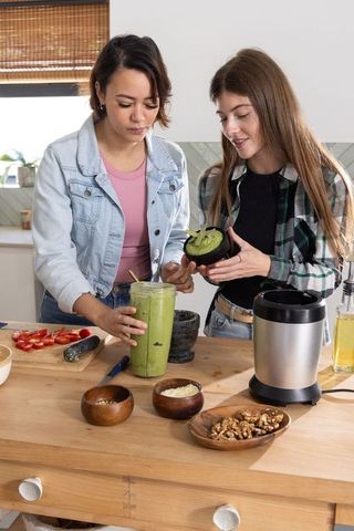 Diverse friends preparing bright green avocado pesto on wooden kitchen island