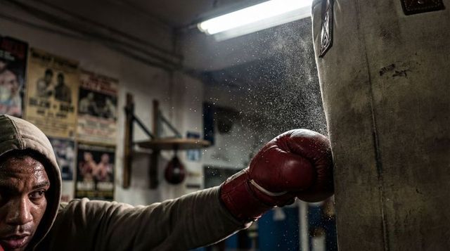 Boxer power punching heavy bag in gritty gym with dust exploding from impact
