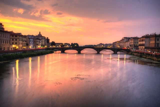 Historic urban bridge over a serene river during a vibrant sunset, ideal for travel and tourism websites, architectural appreciation, serene cityscape illustrations, and brochures showcasing beautiful city destinations.