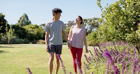 Couple walking hand in hand through sunny garden with purple lavender and smiles