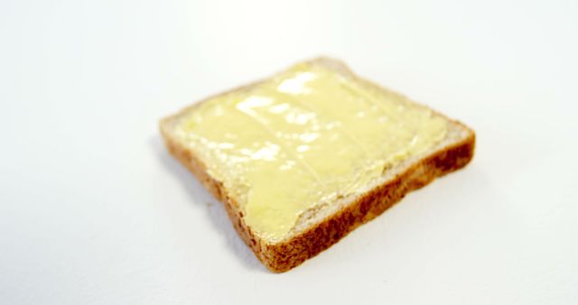 A single slice of bread is spread with butter, set against a plain white background, with copy space. Its simplicity suggests a focus on basic food staples or the concept of a minimalistic meal.