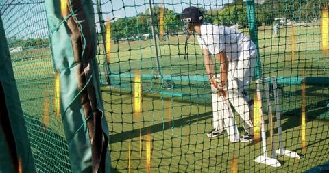 Male cricket batsman practicing in net cage on field