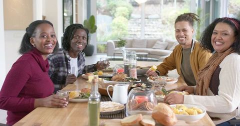 Multiracial friends gathering for cozy brunch around wooden table sharing bread and laughter