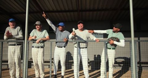 Diverse male baseball teammates cheering and leaning on dugout railing celebrating victory