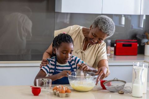 Senior african grandma guiding granddaughter whisking batter and baking together