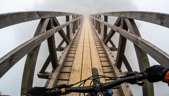 Mountain biking across foggy wooden plank bridge rider pov narrow high-elevation trail