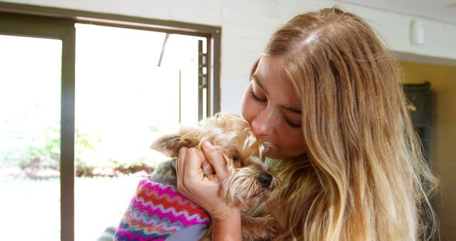 Blonde woman kissing small dog wearing colorful sweater indoors - Download Free Stock Images Pikwizard.com