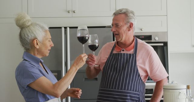Happy caucasian senior couple wearing aprons cooking and drinking wine. active and healthy retirement lifestyle at home.