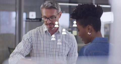 Collaborating colleagues reviewing tablet with user icons on glass in modern coworking