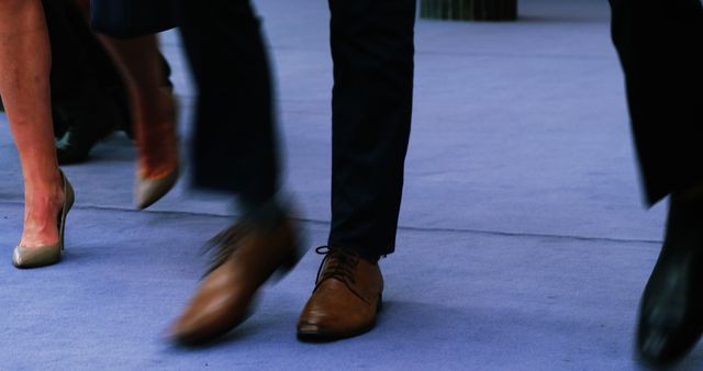 Close-up of business professionals walking on blue carpet, showcasing legs and shoes in motion blur. Useful for content about corporate events, formal meetings, business attire, and professional environments.