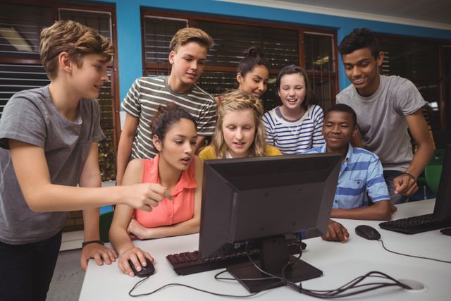Diverse group of students collaborating and studying together in a computer classroom. They are gathered around a computer, smiling and engaged in a group project. Ideal for educational content, teamwork and collaboration themes, and technology in education.