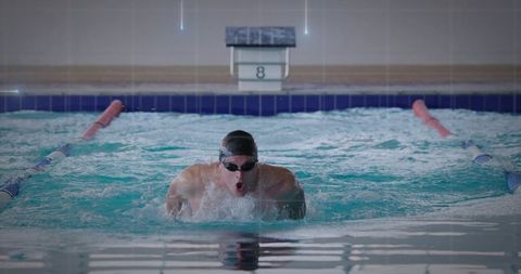 Competitive swimmer pushing through center lane in indoor pool, powerful splash and focus