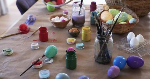 Decorating Easter eggs on craft table with paints, brushes, baskets and pastel eggs