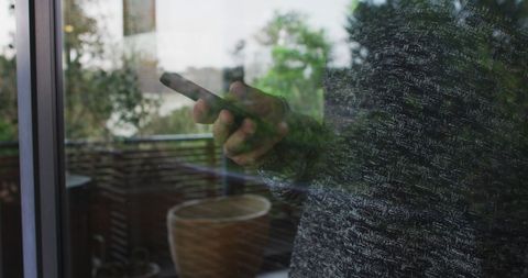 Person using smartphone through reflective window at home