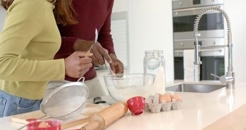 Diverse couple mixing batter and baking together on modern bright kitchen island with eggs