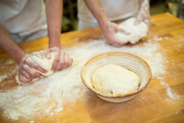 Mid section or two bakers kneading dough on counter