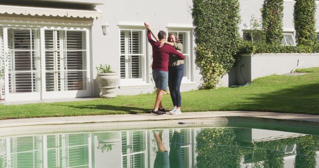 Happy senior caucasian couple dancing by swimming pool in sunny garden. happy, healthy retirement lifestyle at home.